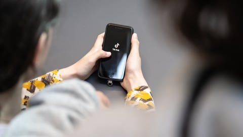 Eine Jugendliche schaut auf ein Handy mit TikTok-Logo - nach einer TikTok-Challenge ist eine Schülerin aus Kaiserslautern ins Krankenhaus gekommen. (Foto: dpa Bildfunk, picture alliance/dpa | Hannes P. Albert)